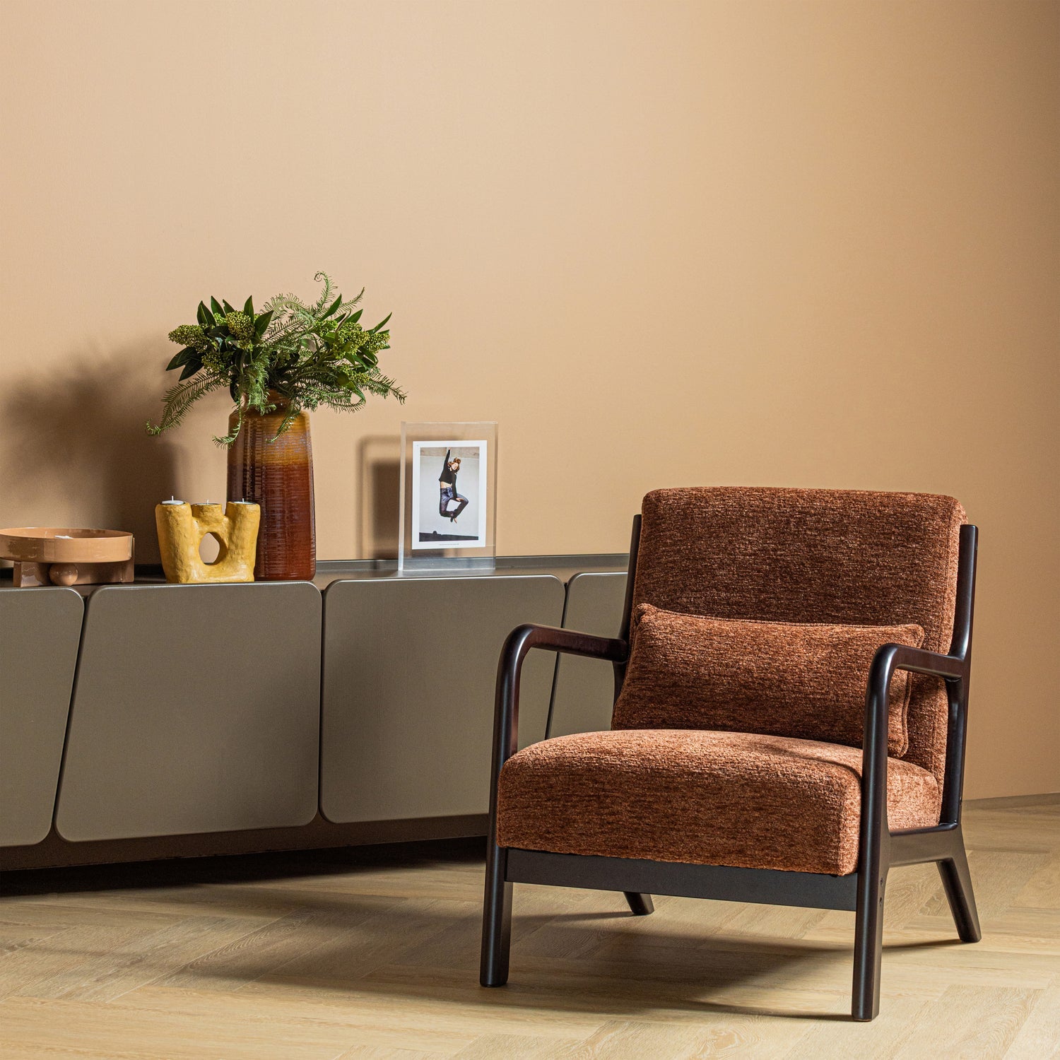 Bruine chenille fauteuil met donker frame, armleuningen en brede zitting.