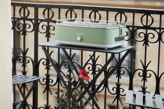 Groene elektrische tafelgrill op balkon met metalen rooster en deksel