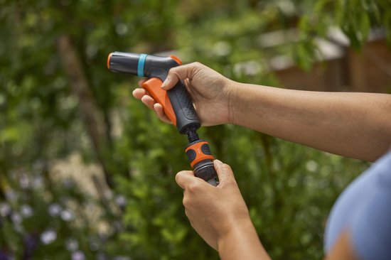 Spuitpistool met oranje trekker in hand, waterstraal gericht op groen