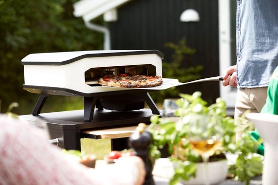 Elektrische pizzaoven met pizza op steen, open, wit ombouw en zwarte pootjes.