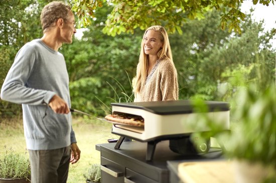 Elektrische pizzaoven op terras, wit ombouw en zwarte basis met open voorkant.