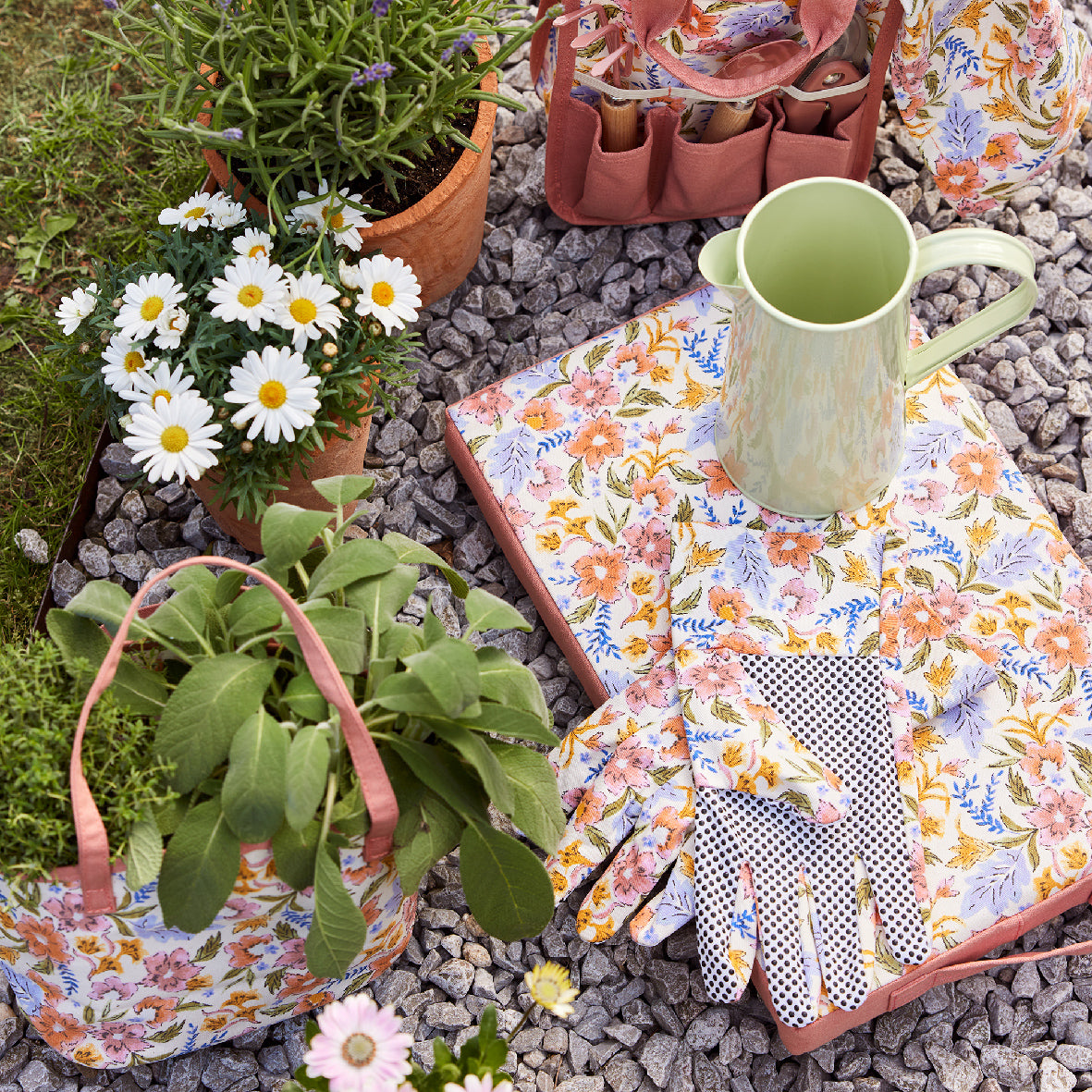Tuingereedschapsset met roze gereedschapshouders, bloemige handschoenen en spatel op grind