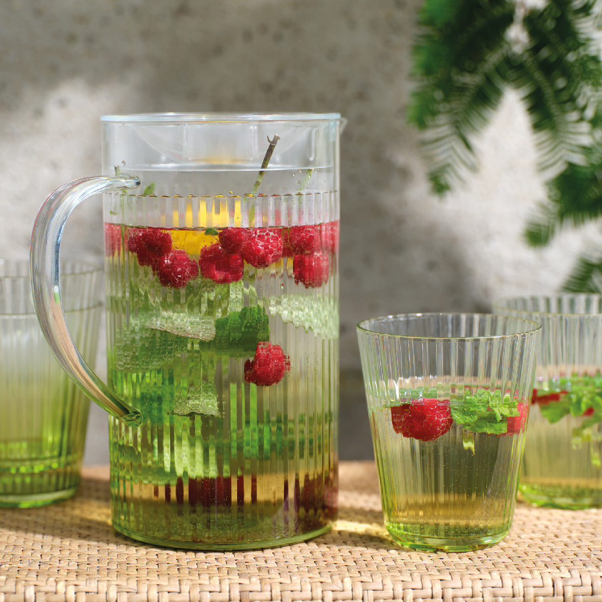 Gevulde plastic kruik met groene drank en frambozen, met 1 glas ernaast