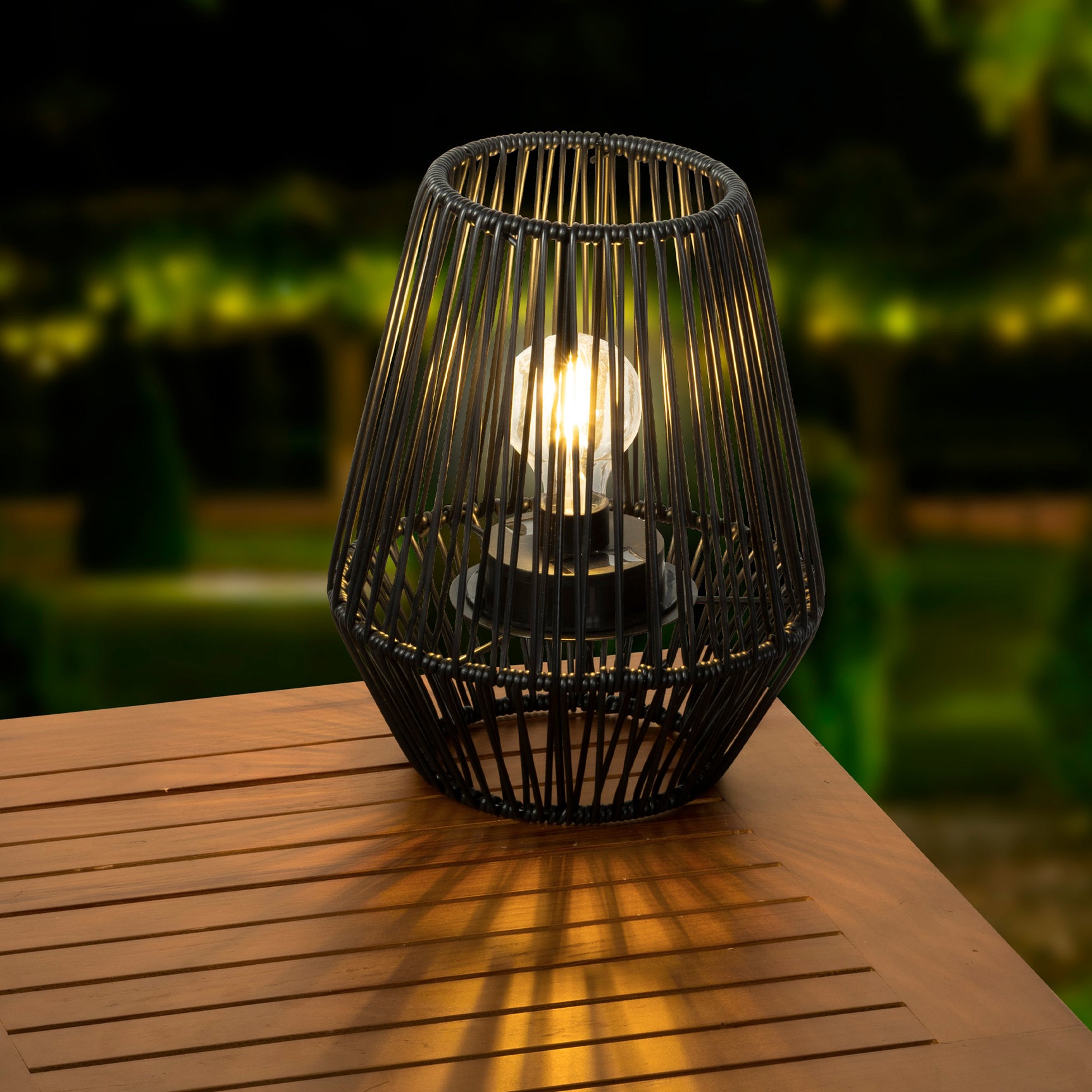 Solarlantaarn van zwart riet met brandende kaarslamp op houten plank