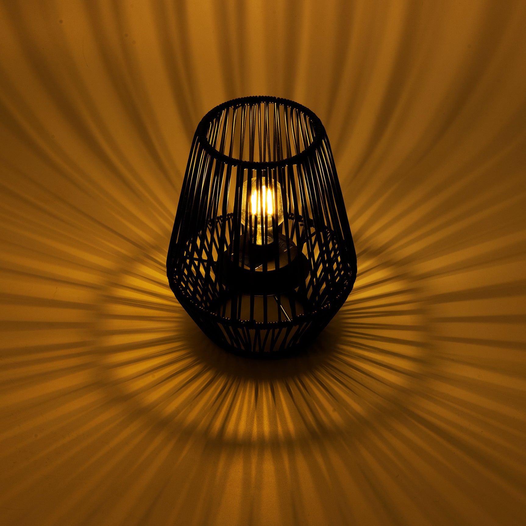 Solarlantaarn van zwarte rieten kooi met brandende kaarslamp en lichtstralen