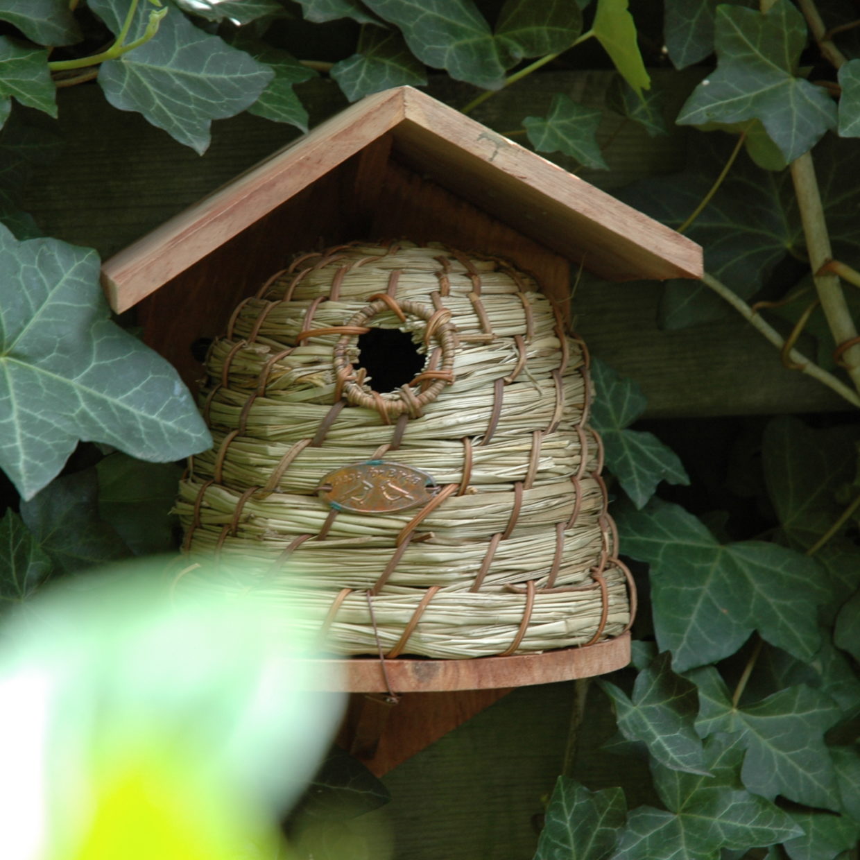 Houten bijenhuis met stro-gevlochten nestkamer en ronde ingang, dak open