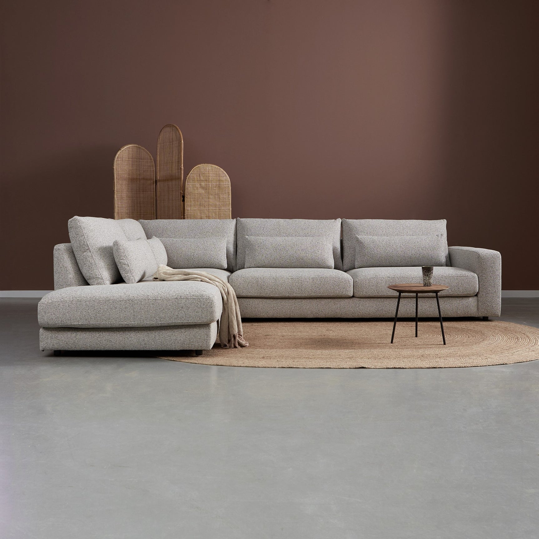 Loungebank met chaise links, lichtgrijze stof, losse kussens en plaid op de zitting