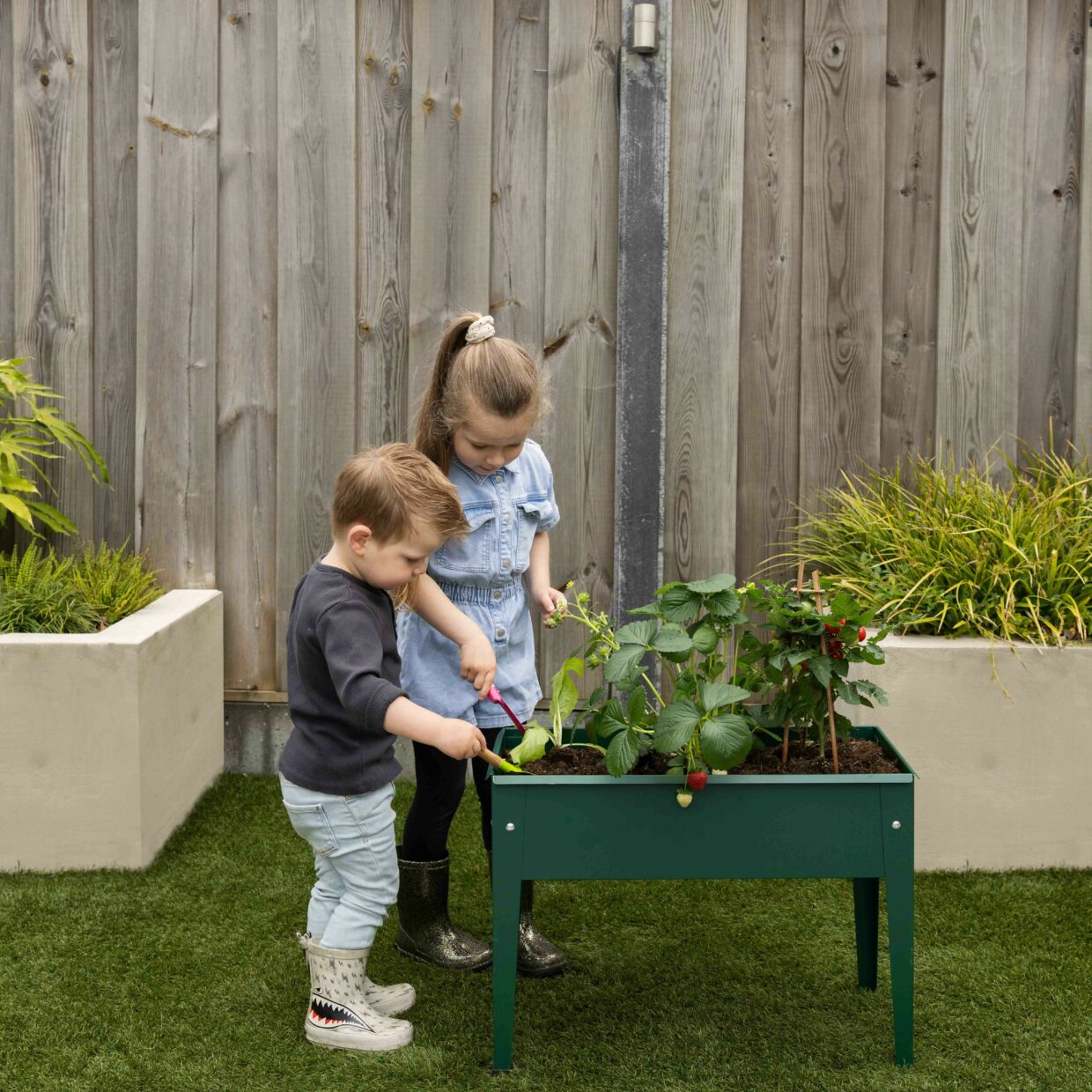 Groene verhoogde metalen kweekbak in tuin, met kinderen die planten verzorgen
