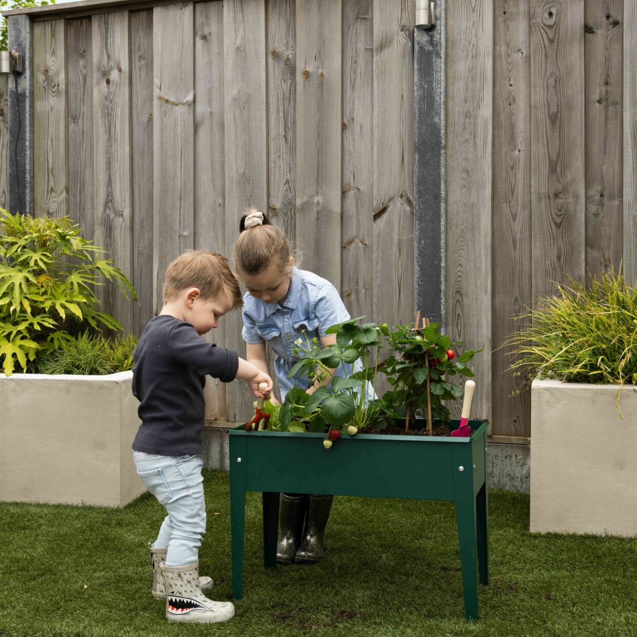 Groene verhoogde metalen kweekbak met planten, kinderen bezig in de tuin
