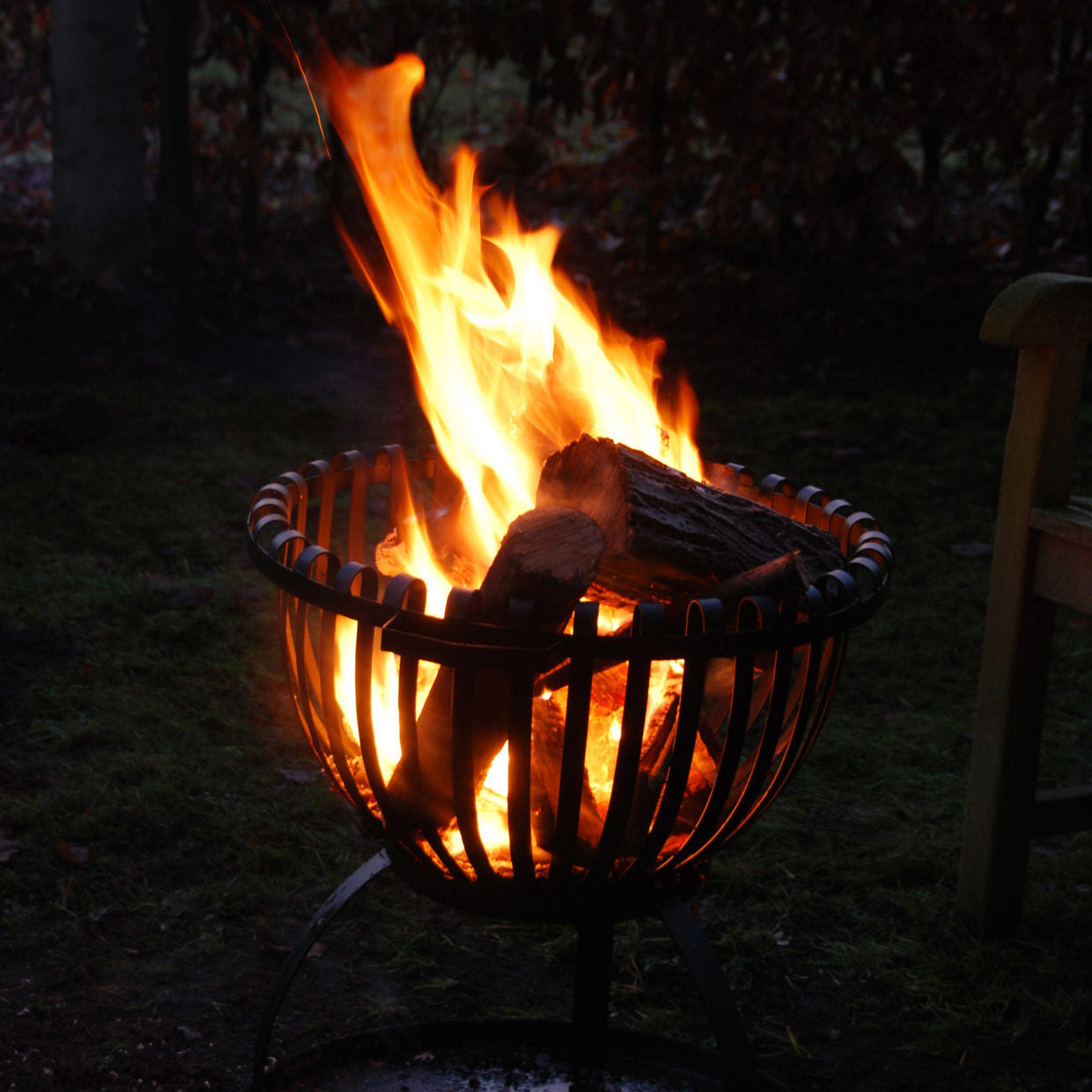 Tulpvormige vuurkorf met brandende vlammen en houtblokken, zwarte metalen spijlen