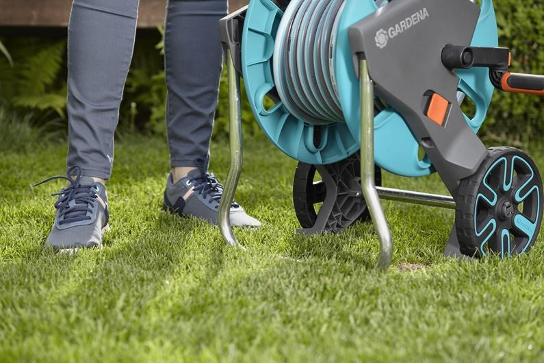 Gardena slangenwagenhaspel op gras, turkoois en grijs met oranje knop, wielen links