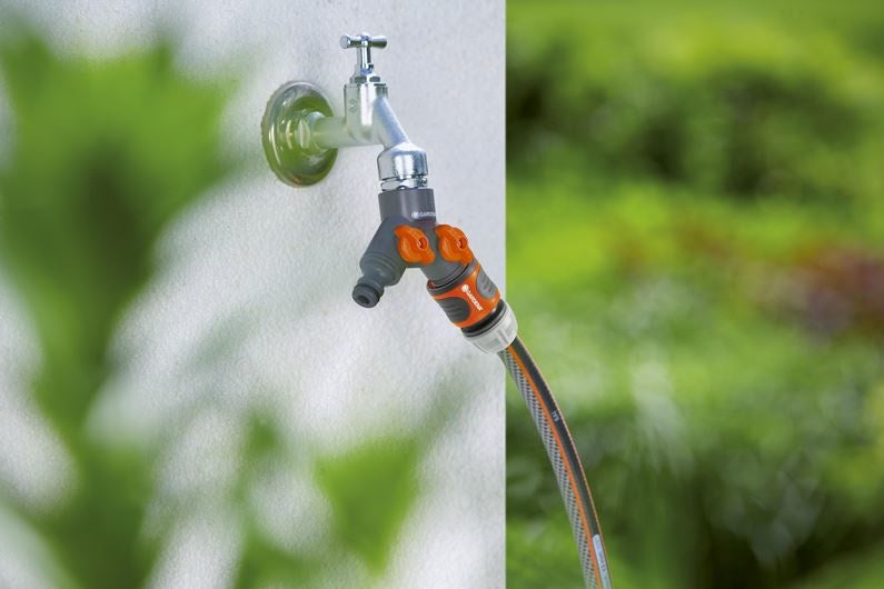 Gardena 2-wegstuk 3/4" met oranje knoppen en twee slanguitgangen, aangesloten op kraan