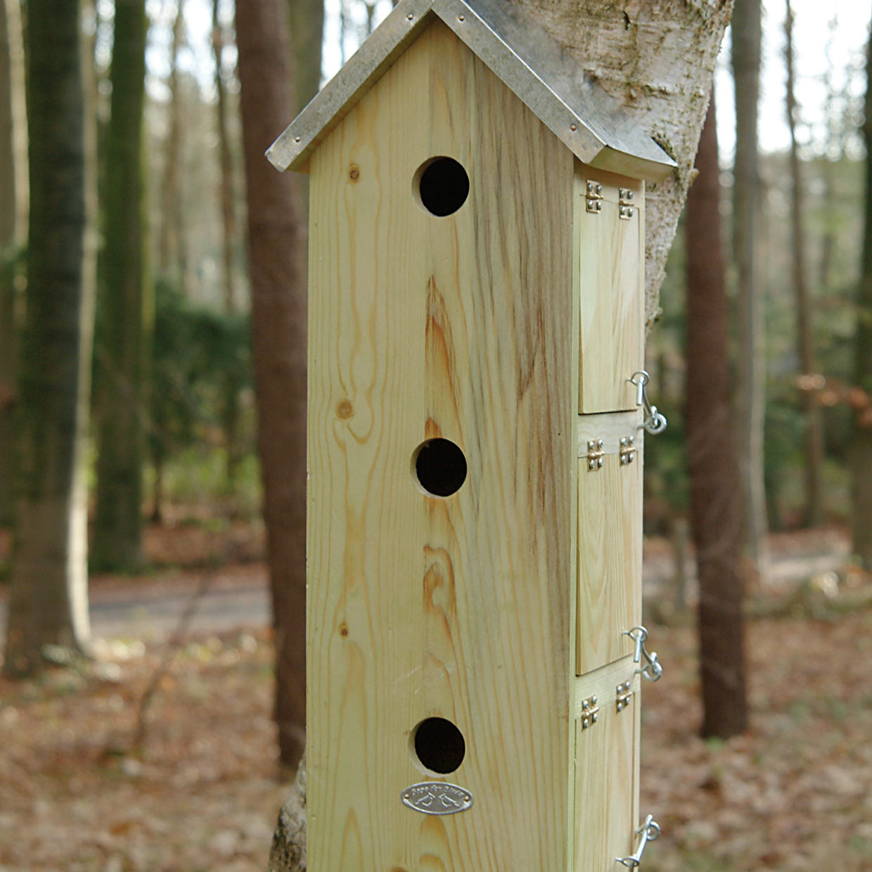 Houten vogelhuisje met grijze dak en drie ronde ingangen, metalen deur en haken