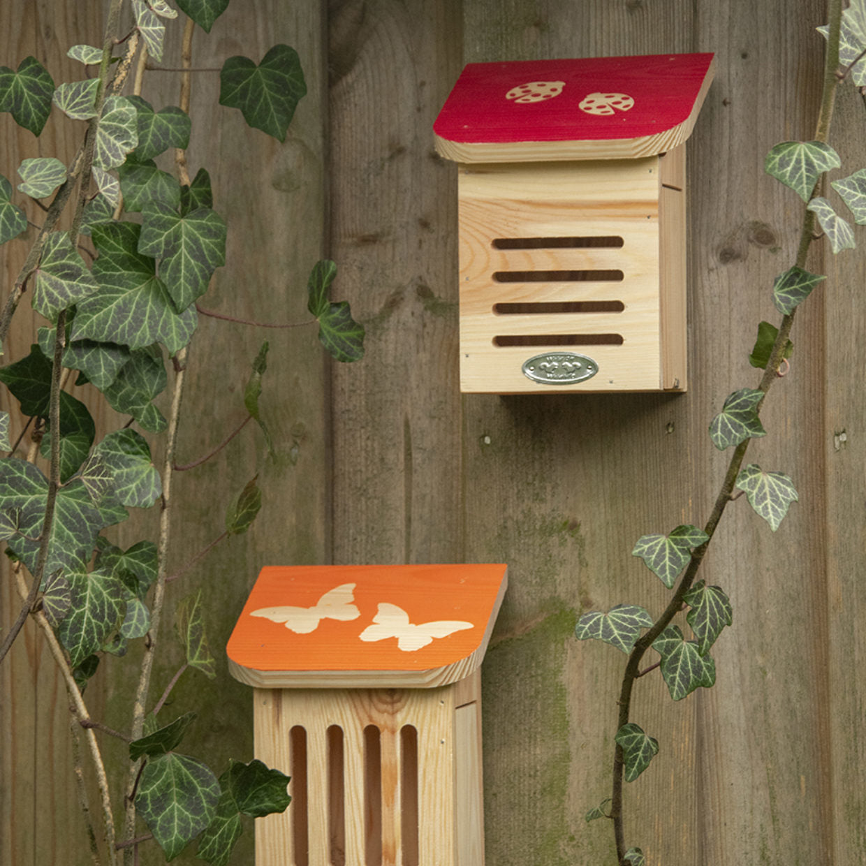 Twee houten lieveheersbeestjeshuizen aan wand, met rood en oranje daken.