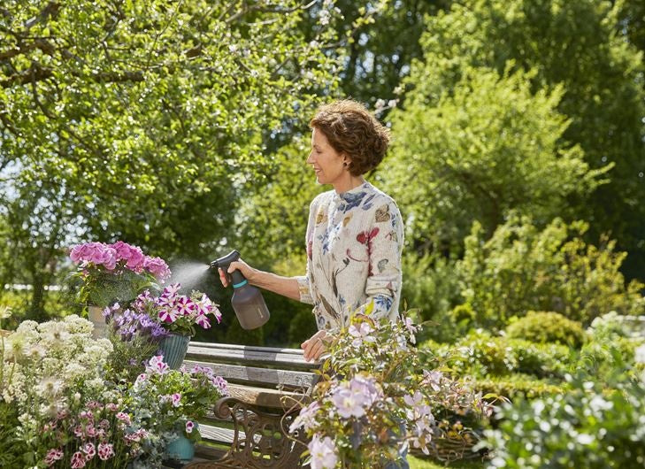 Gardena plantenspuit in de tuin, donkergrijze spuitfles met blauwe band en trekker