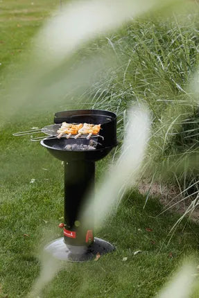 Zwarte houtskoolbarbecue met rooster en brandende kolen, op een poot in het gras