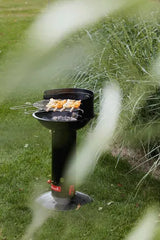 Zwarte houtskoolbarbecue met rooster en brandende kolen, op een poot in het gras
