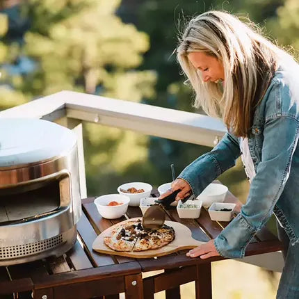 Pizzasnijder met metalen wieltje in hand op pizza op grillplank