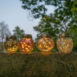 Vier glazen zonne-LED lantaarns met amberkleurig licht, op steen
