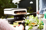Elektrische pizzaoven met pizza op steen, open, wit ombouw en zwarte pootjes.