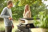 Elektrische pizzaoven op terras, wit ombouw en zwarte basis met open voorkant.