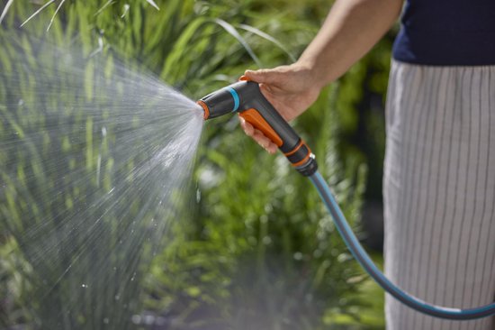 Spuitpistool met oranje trekker aan tuinslang, waterstraal richting beplanting