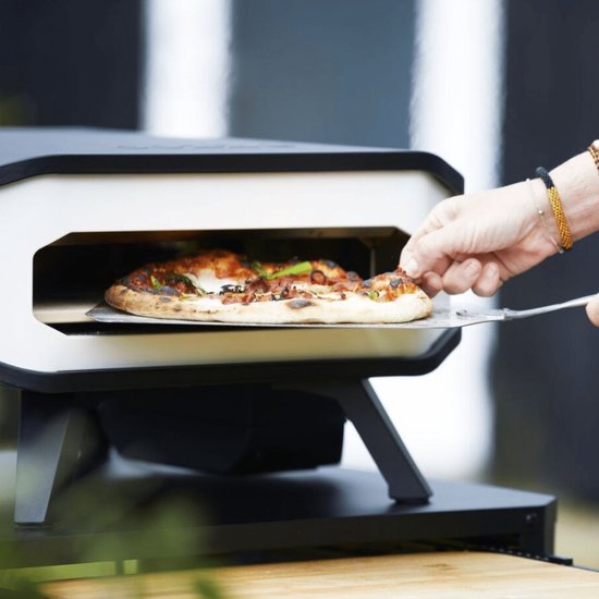Elektrische pizzaoven met pizza op steen, hand met schep, wit ombouw en zwart.