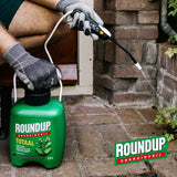Groene RoundUp onkruidbestrijder-sprayfles in gebruik, spuitstraal naast bestrating
