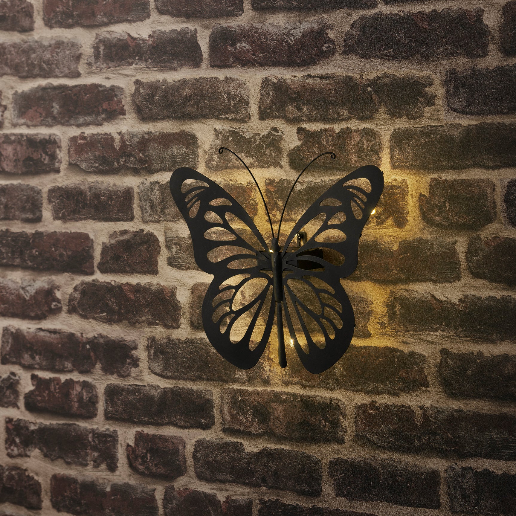 Vlinder wandlamp van ijzer met licht dat door de vleugels schijnt.