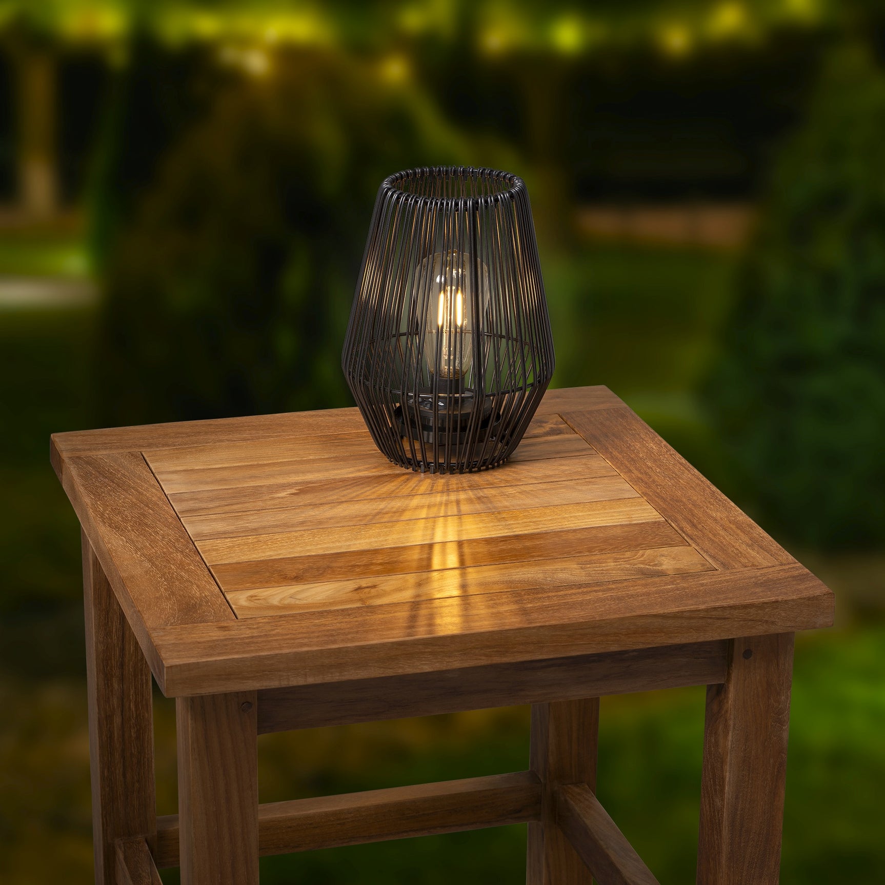 Zonne-lantaarn van wicker met glazen cilinder, op houten tafel