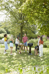 Zwarte houtskoolbarbecue op poot met rond rooster, in een tuin met gras