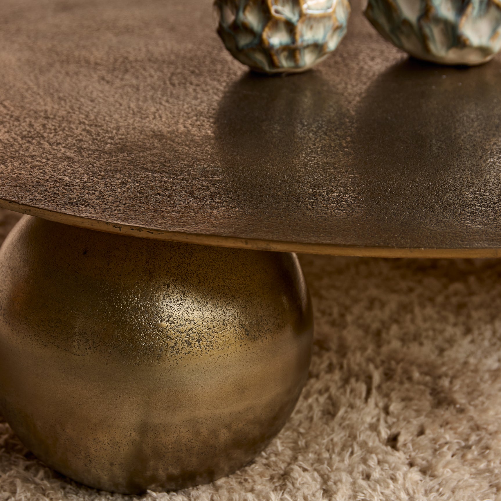 Ronde salontafel met donker goudkleurig blad en massieve bolvormige poot