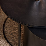 Zwart tafelblad met afgeronde rand en metalen poot, close-up.