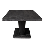 Zwarte eettafel met massief blad en taps toelopende centrale poot op onderstel.