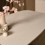 Ovale eettafel met zandkleurig blad, afgeronde hoek en tafelrand in zicht