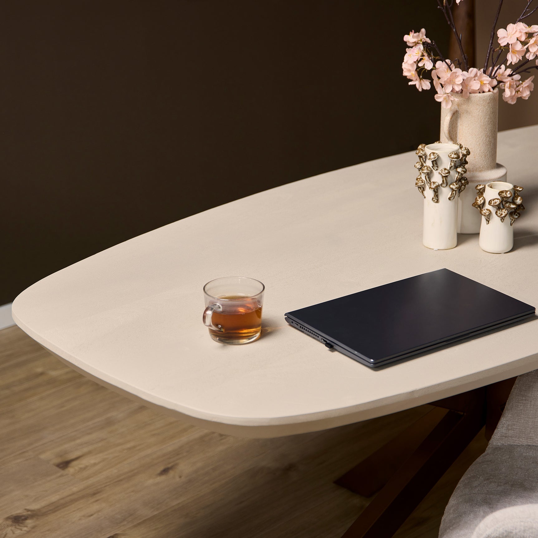 Ovale eettafel in zandkleur met afgeronde randen; tafelblad met mokken en tablet
