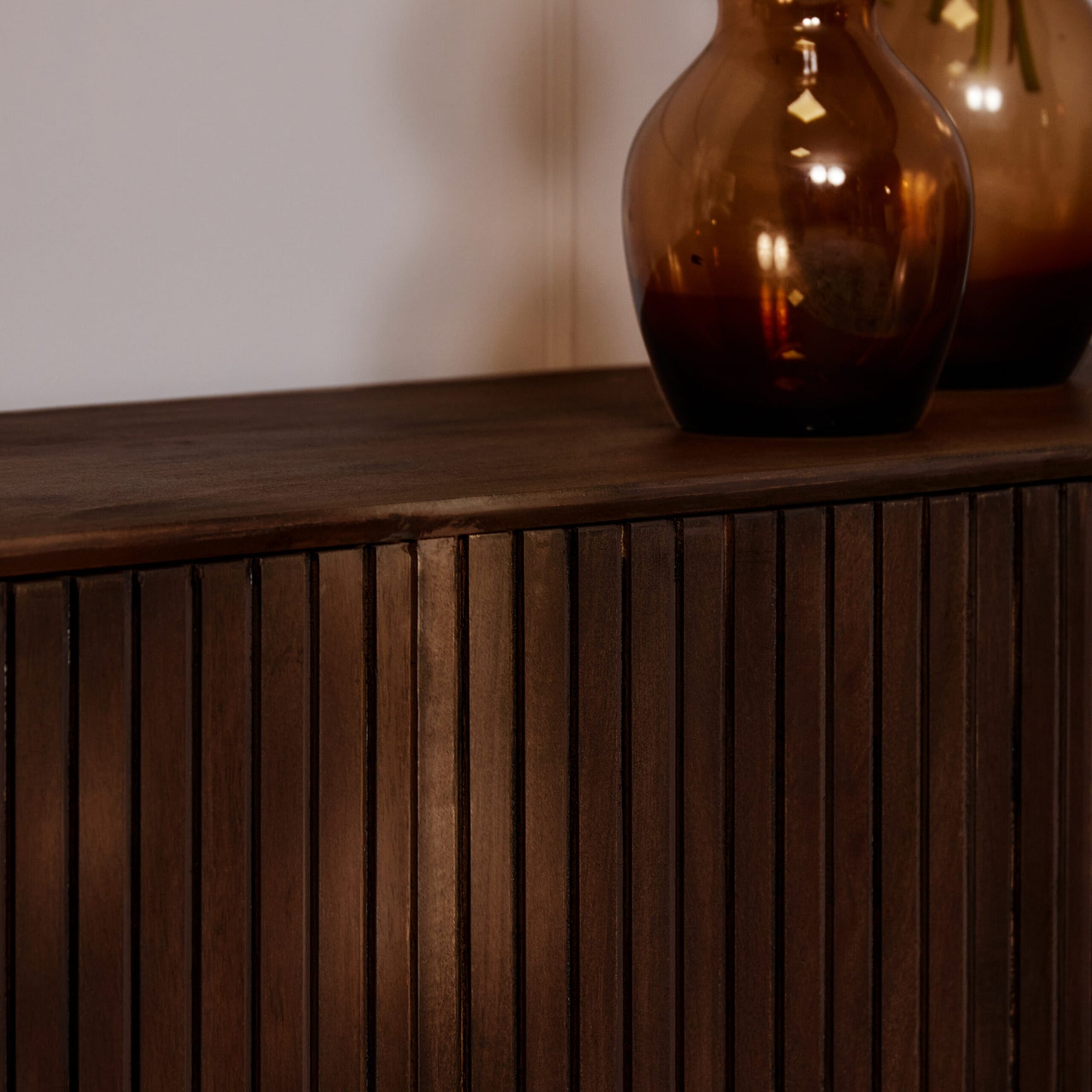 Tv-meubel houtfront met verticale groeven en strakke afwerking; bovenblad met donkernerfde rand.