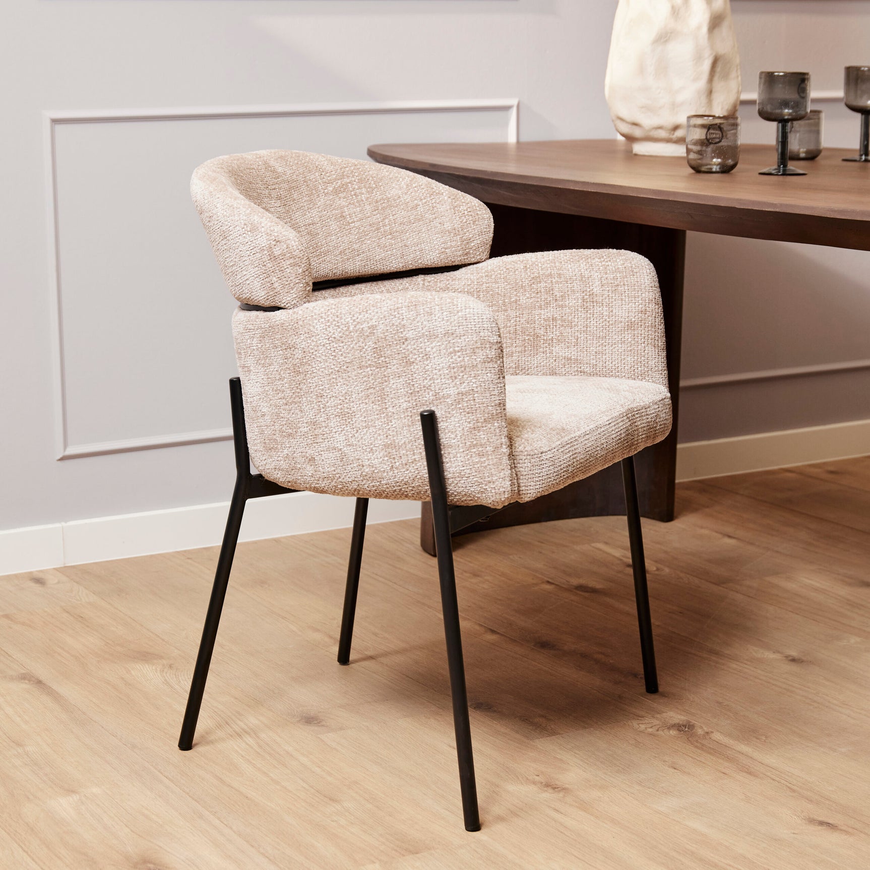 Beige eetkamerstoel met dikke armleuning, afgeronde rug en zwarte metalen poten