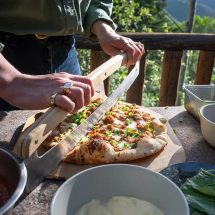 Pizza snijblad in gebruik op gegrilde pizza, houten handgreep