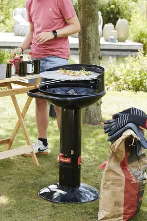 Zwarte houtskoolbarbecue op poot met open deksel, buiten in de tuin