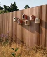 Meerdere rode vogelhuisjes met rond invlieggat, bevestigd op een verticale plank.
