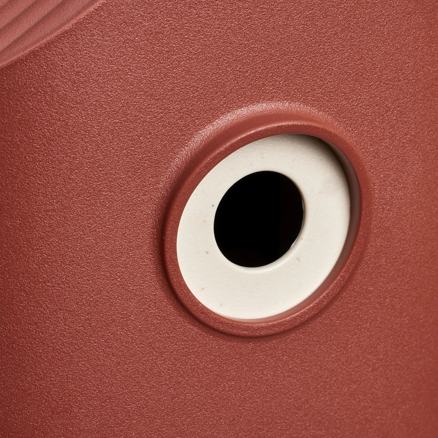 Rond invlieggat van rood vogelhuis met witte omlijsting en zwarte opening.