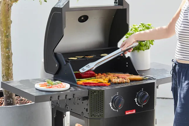 Gasbarbecue met open deksel en rooster met etenswaren, hand met tang